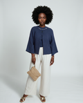 Woman wearing a blue top and white pants with a beige clutch against a white background